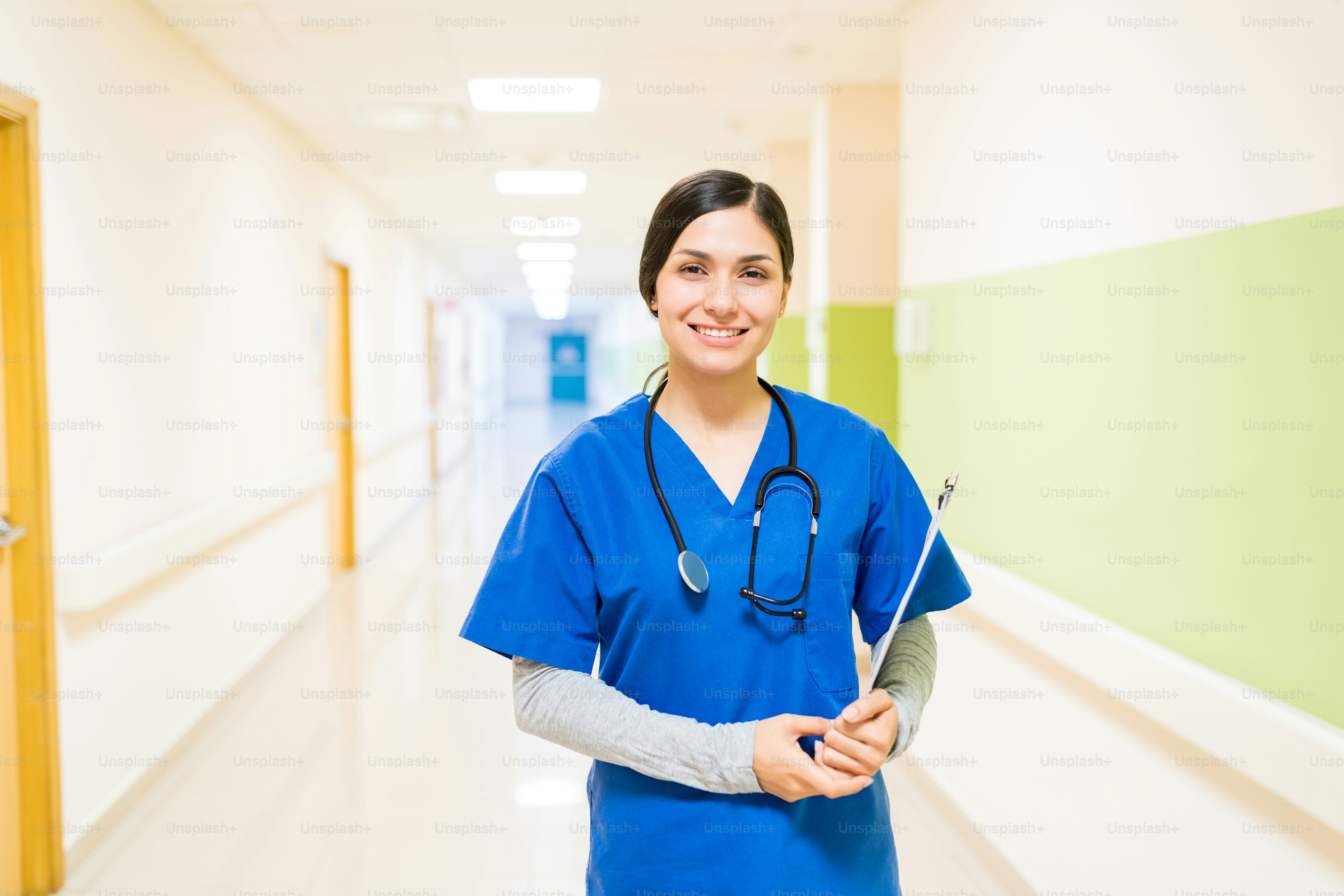 Latin young female doctor with stethoscope and clipboard wearing shrubs standing in corridor at hospital